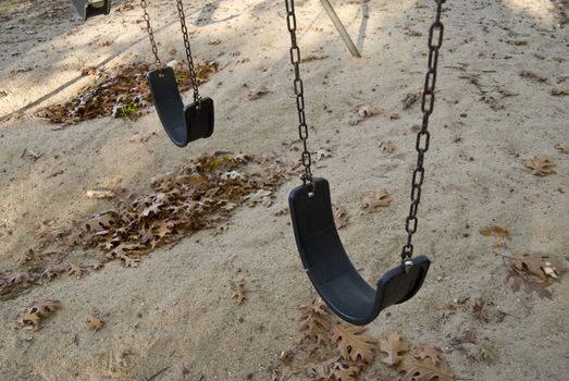 Some empty playground swings at the park.