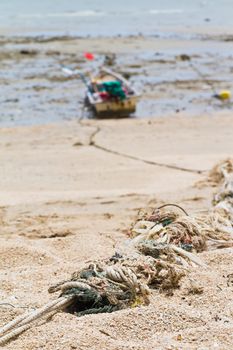 Rope tied to a fishing boat on the beach near the ocean in view.