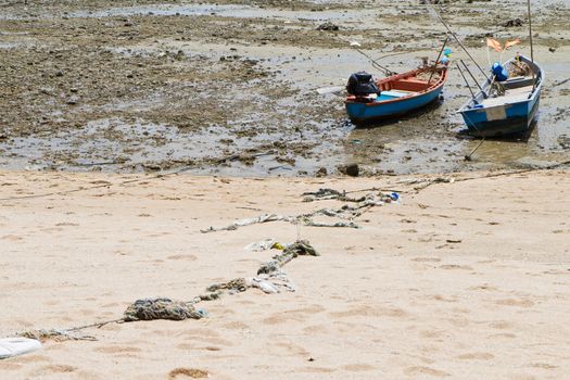 Rope tied to a fishing boat on the beach near the ocean in view.