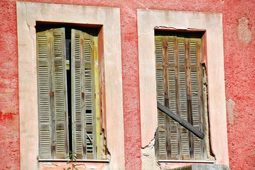 Boarded up window shutters and weathered red wall. Abandoned house detail.