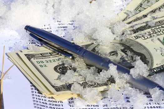 cold frosted dollar bill stuck in cold snow with spreadsheet.