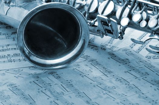 Old saxophone and notes. The Musical instrument laying on notes with classical music of the beginning of 17 centuries