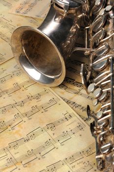 Old saxophone and notes. The Musical instrument laying on notes with classical music of the beginning of 17 centuries