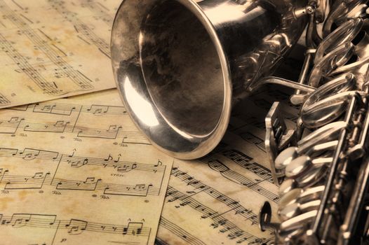 Old saxophone and notes. The Musical instrument laying on notes with classical music of the beginning of 17 centuries
