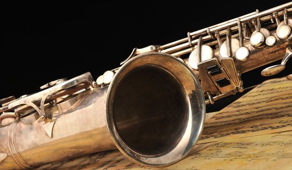 Old saxophone and notes. The Musical instrument laying on notes with classical music of the beginning of 17 centuries