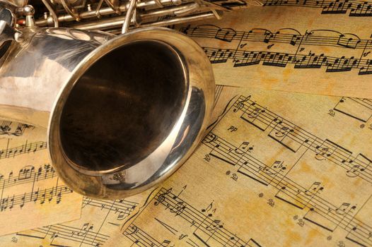 Old saxophone and notes. The Musical instrument laying on notes with classical music of the beginning of 17 centuries