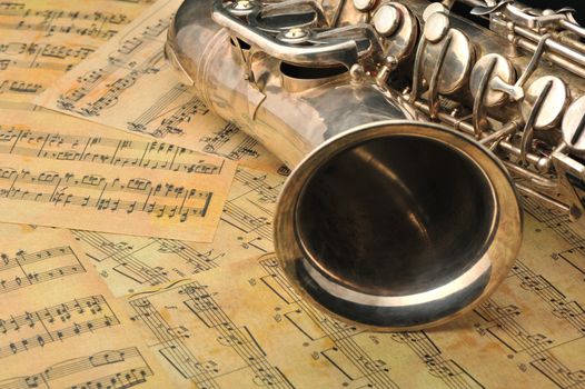 Old saxophone and notes. The Musical instrument laying on notes with classical music of the beginning of 17 centuries