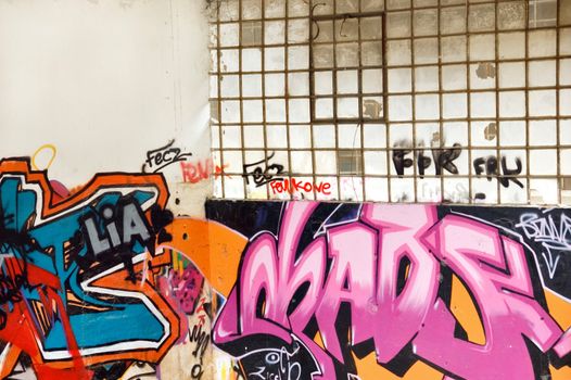 Graffiti covered wall and broken windows inside a partially demolished factory.