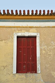 Red window shutter and weathered wall of a neoclassical building in Athens, Greece.