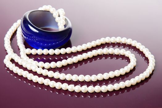 Pearl necklace and blue bracelet over glossy purple background