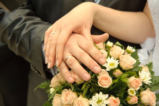 Hands of a newly-married couple. Tenderness of the groom and the bride above wedding a bouquet