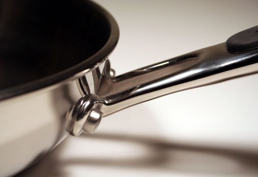 A close up of the handle of a stainless steel frying pan.