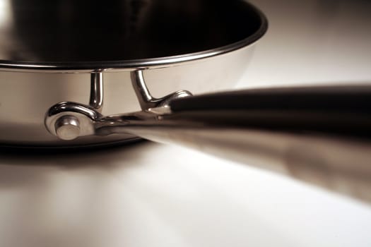 A close up of the handle of a stainless steel frying pan.
