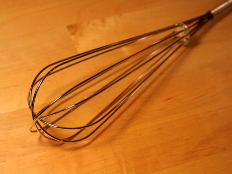 A whisk sitting on a wooden table.