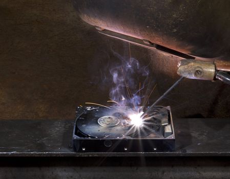 repairing a defect hard disk with welding apparatus. Protective shield and smoke on rusty background