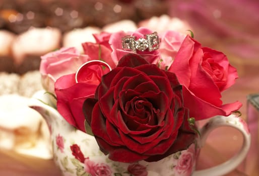 Small bouquet of red and pink roses in a vase with two wedding rings on top. Very shallow depth of field, macro shot