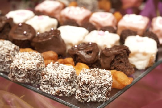 Selection of miniature petit-fours - coconut, chocolate cream, strawberry and vanilla cakes on glass plate