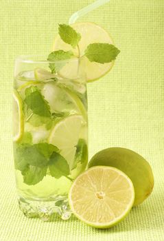 Mojito cocktail with lime, mint leaves and ice on green mesh background