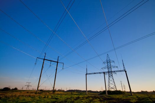 Electric power lines in a field over blue morning sky with many crossing wires. Horizontal