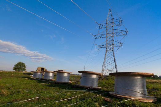 A power line tower in the field and five bobbins with aluminum wire ready to installation