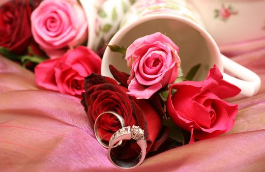 Small bouquet of red and pink roses in a vase with two wedding rings. Very shallow depth of field, macro shot