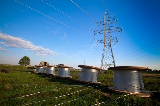 A power line tower in the field and five bobbins with aluminum wire ready to installation