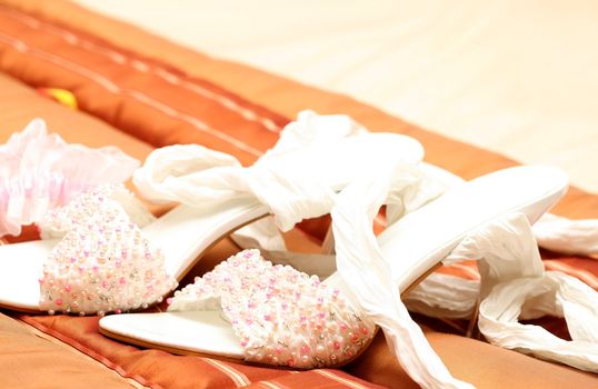 White bridal shoes adorned with pink, white and silver beads lying on brown bed cover