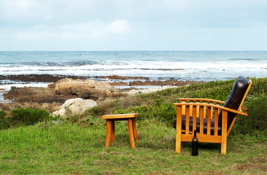 Wooden chair standing outside by the ocean on a sunny summer day with blue skies and waves in the background