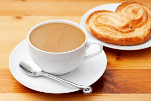 Closeup of coffee with milk in white cup and a palmier pastry. Shot on light wood background