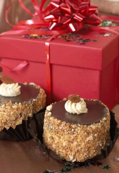 Miniature chocolate meringue cakes with cream and almonds and red gift boxes in the background