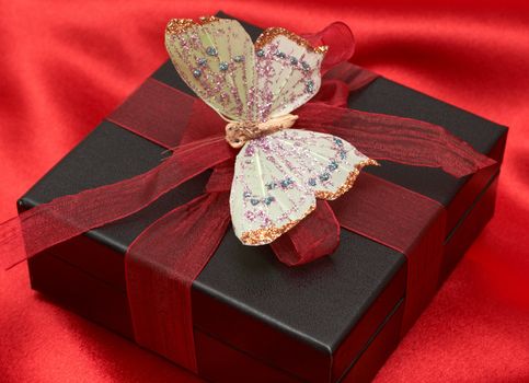 Valentines gift box with red ribbon and colorful butterfly on red silk