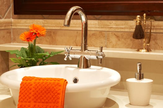 Beautiful sink in a bathroom with towel on it and a flower. Focus is on the tap