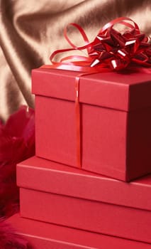 Stack of red gift boxes with bows and feathers on golden silk background