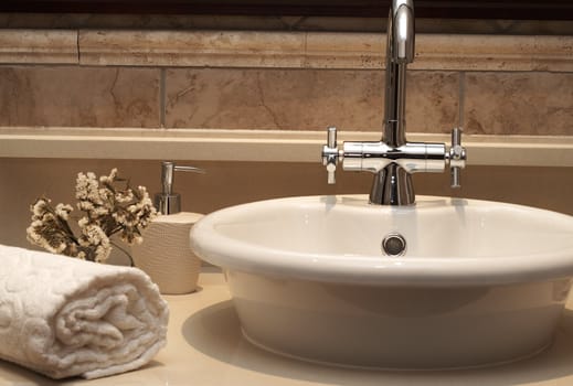 Beautiful sink in a bathroom with rolled up towel next to it and flowers