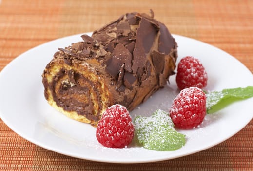 Miniature chocolate swiss roll cake served on a plate with mint leaves and raspberries on orange background