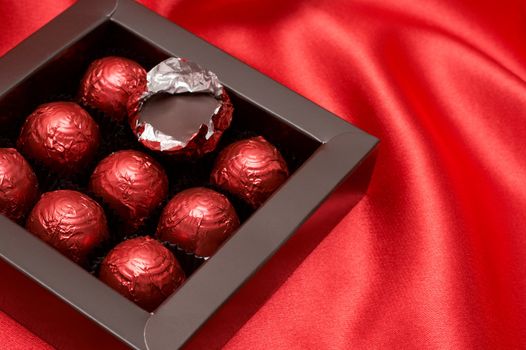 Chocolate Valentines truffles wrapped in red paper on silk material background