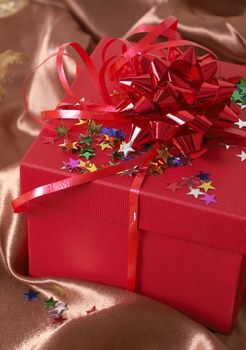 Red gift box with bows and stars on golden silk background