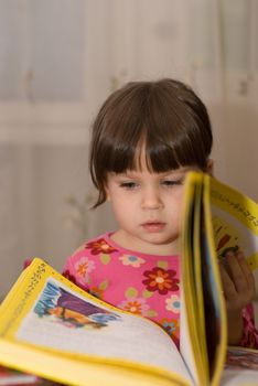 The child reading the book. The three-year girl in house conditions