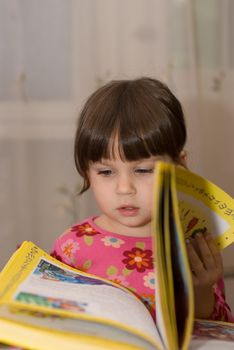 The child reading the book. The three-year girl in house conditions