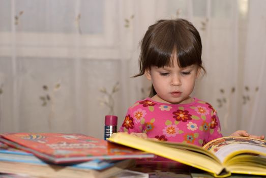 The child reading the book. The three-year girl in house conditions