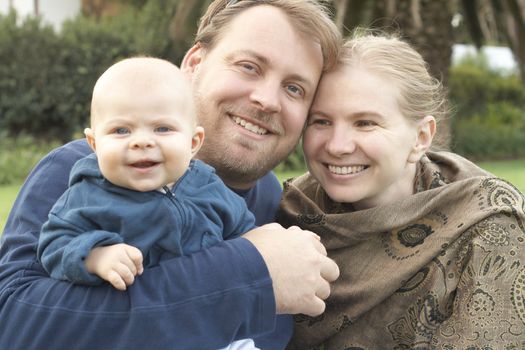 Beautiful happy family of three posing in their garden laughing. Focus is on the father