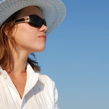 The woman in glasses and a hat on a background of the sky. The adult girl in white clothes