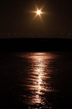 a night view of windmills on the coast