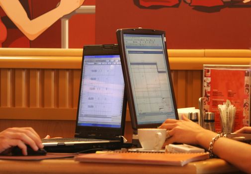 Two persons in cafe work behind computers