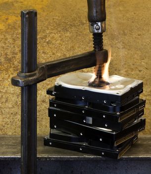 clamp pressing on a stack of hard drives with fire. The top drive is deformed