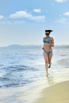 The girl running on seacoast. The European appearance in sunglasses