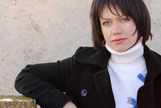 The girl on a background of a dirty wall. The European nationality a black coat