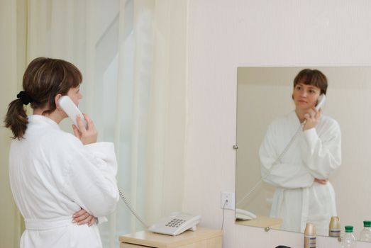 The girl talking by phone. After morning douche in a white dressing gown