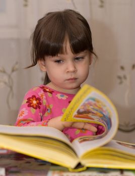 The child reading the book. The three-year girl in house conditions