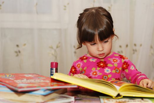 The child reading the book. The three-year girl in house conditions